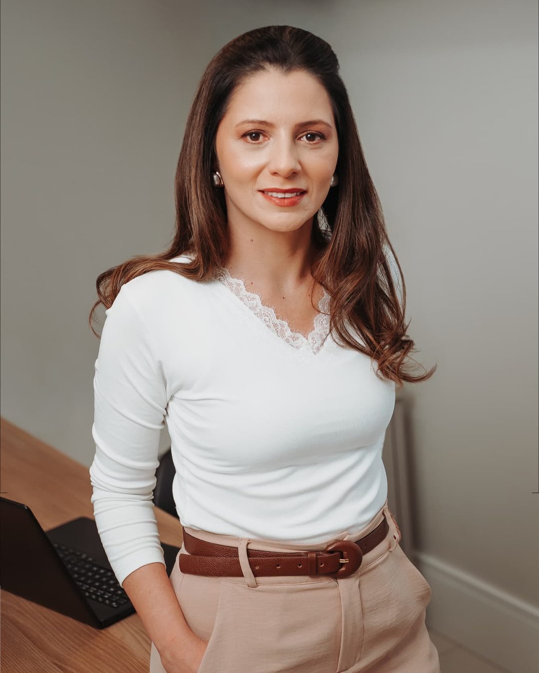 Fabiana Zanuzzo, nutricionista, em pé no consultório, de blusa branca, ao lado da mesa de atendimento.